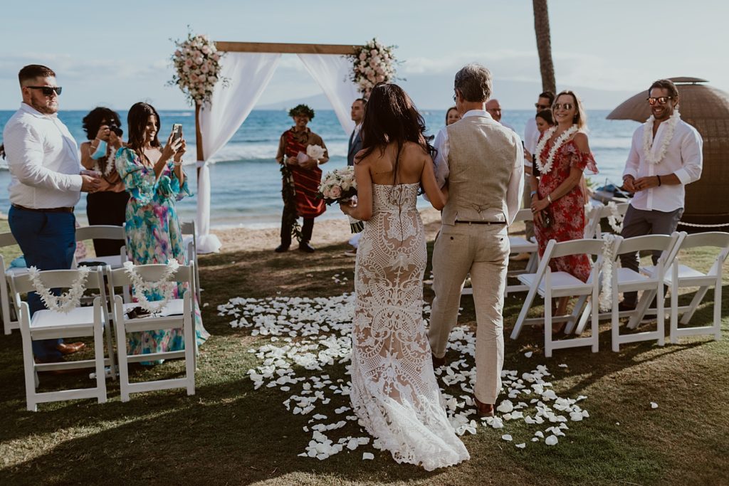 Bride arm in arm with father entering beach Ceremony