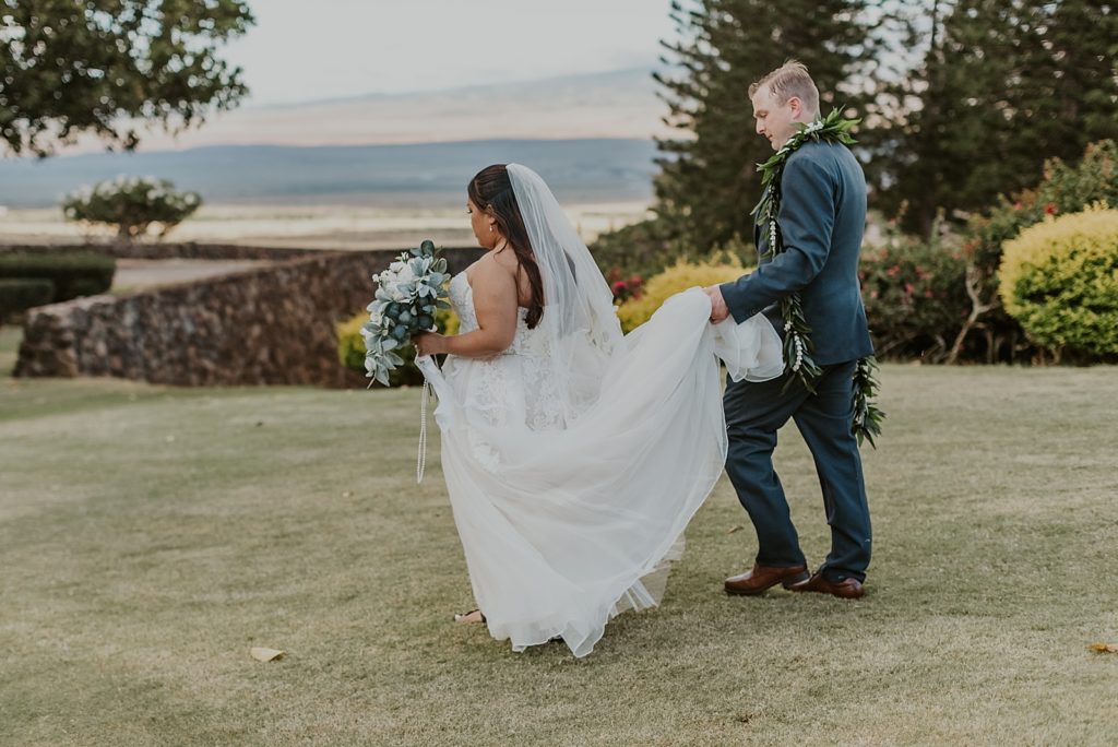 Groom holding Bride's train helping her walk across golf green