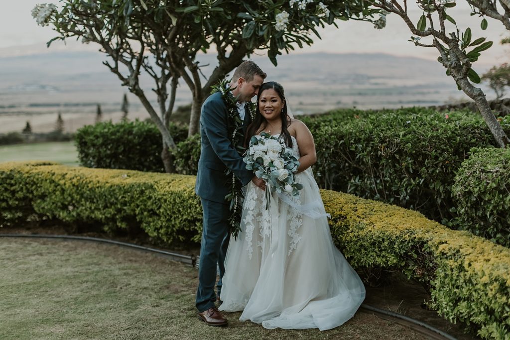 Groom nuzzling Bride outdoor by the greenery