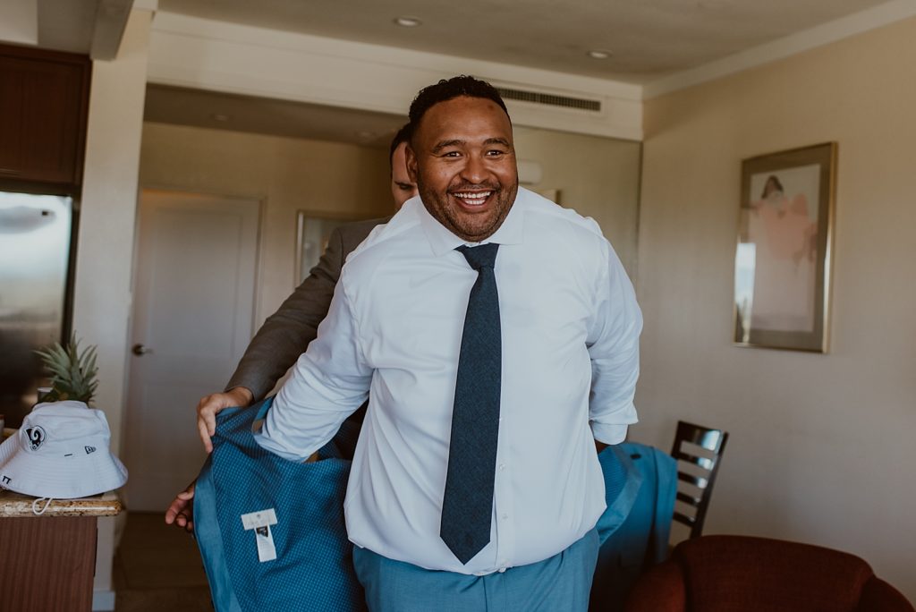 Groom getting help putting on blue jacket getting ready