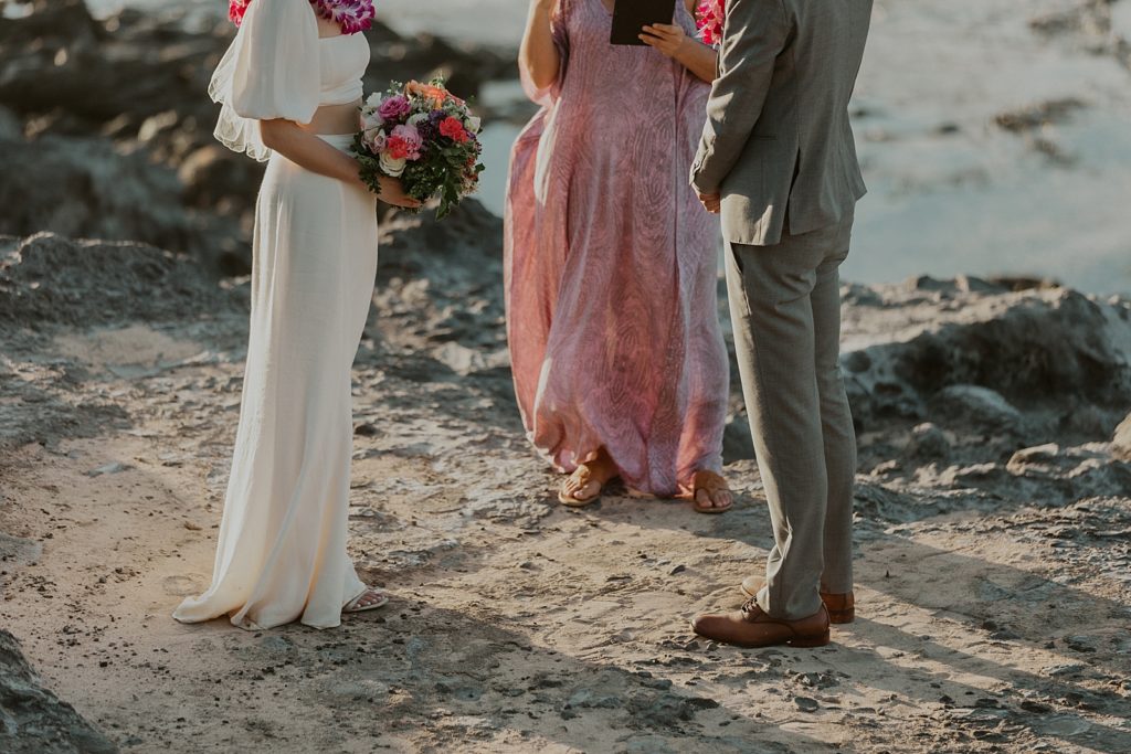 Lower part of Bride and Groom standing with officiant on rocky ground