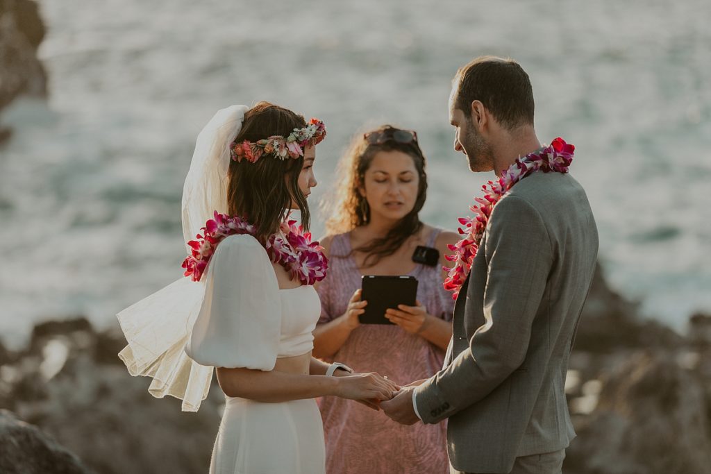 Bride and Groom hand in hand listening to Officiant in front of water