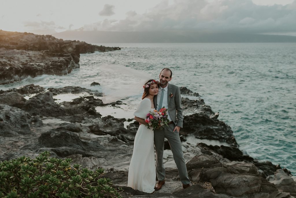 Bride and Groom arms around each other on rocky coast