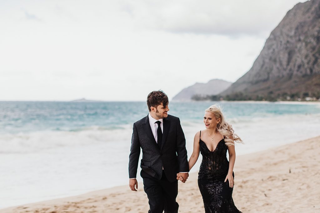 Groom looking at Bride and holding hand as they walk on the shoreline