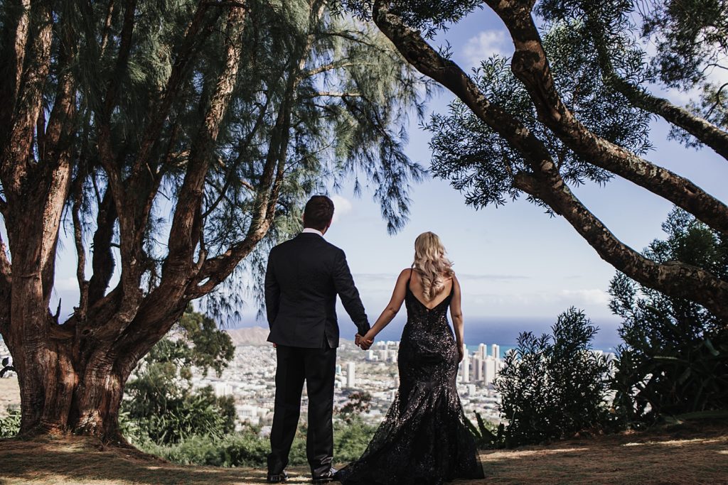 Bride and Groom holding hands looking out at the city from the forest