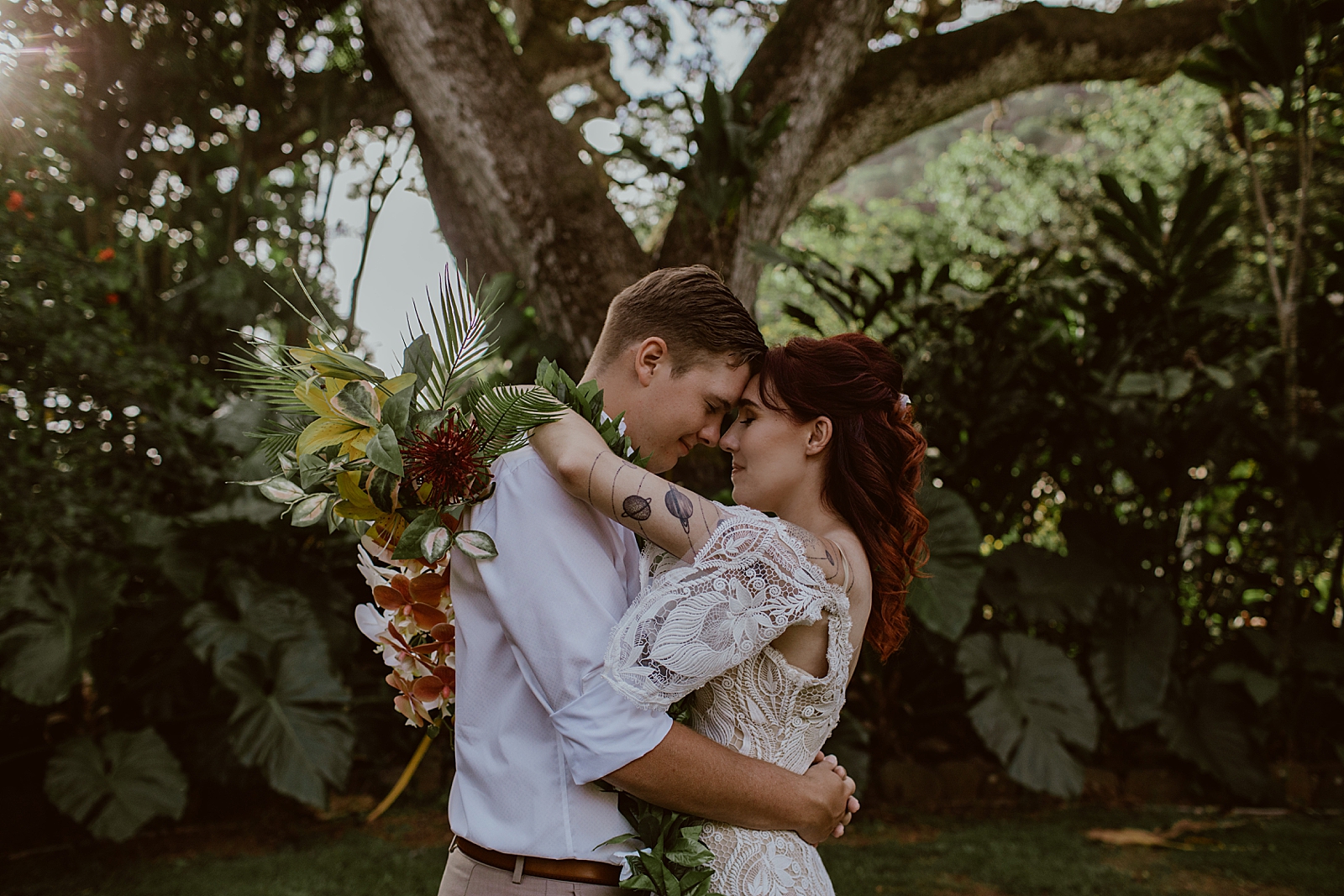 Bride and Groom resting their heads on each other in front of tree