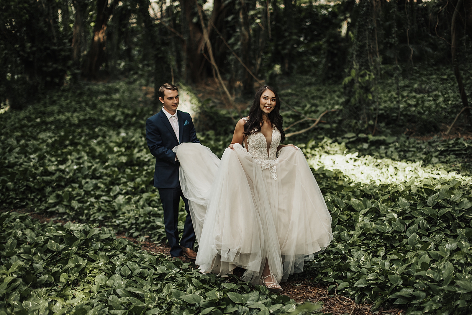 Bride walking holding up wedding dress train and Groom holding back of wedding train