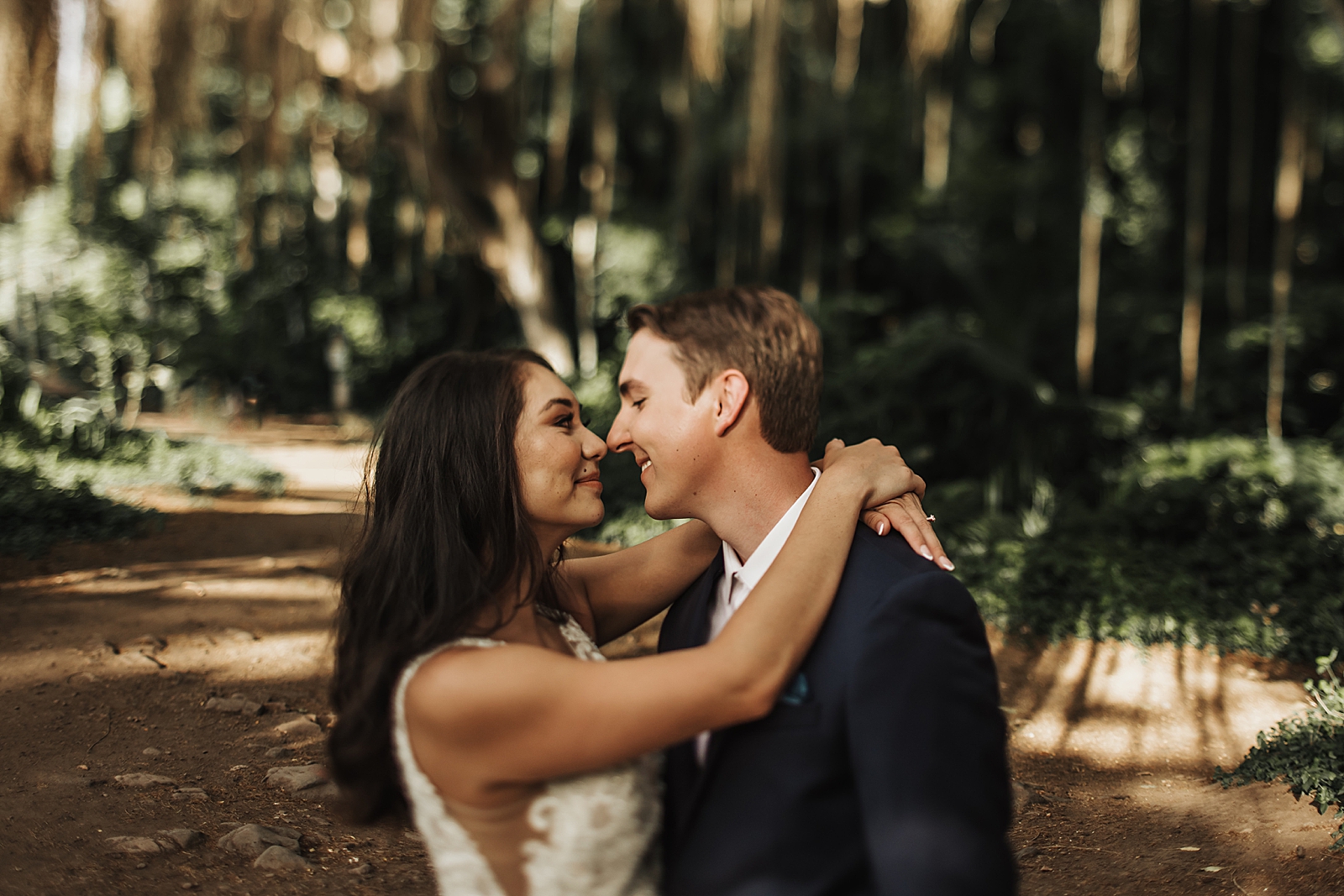 Bride holding Groom and touching noses in forest