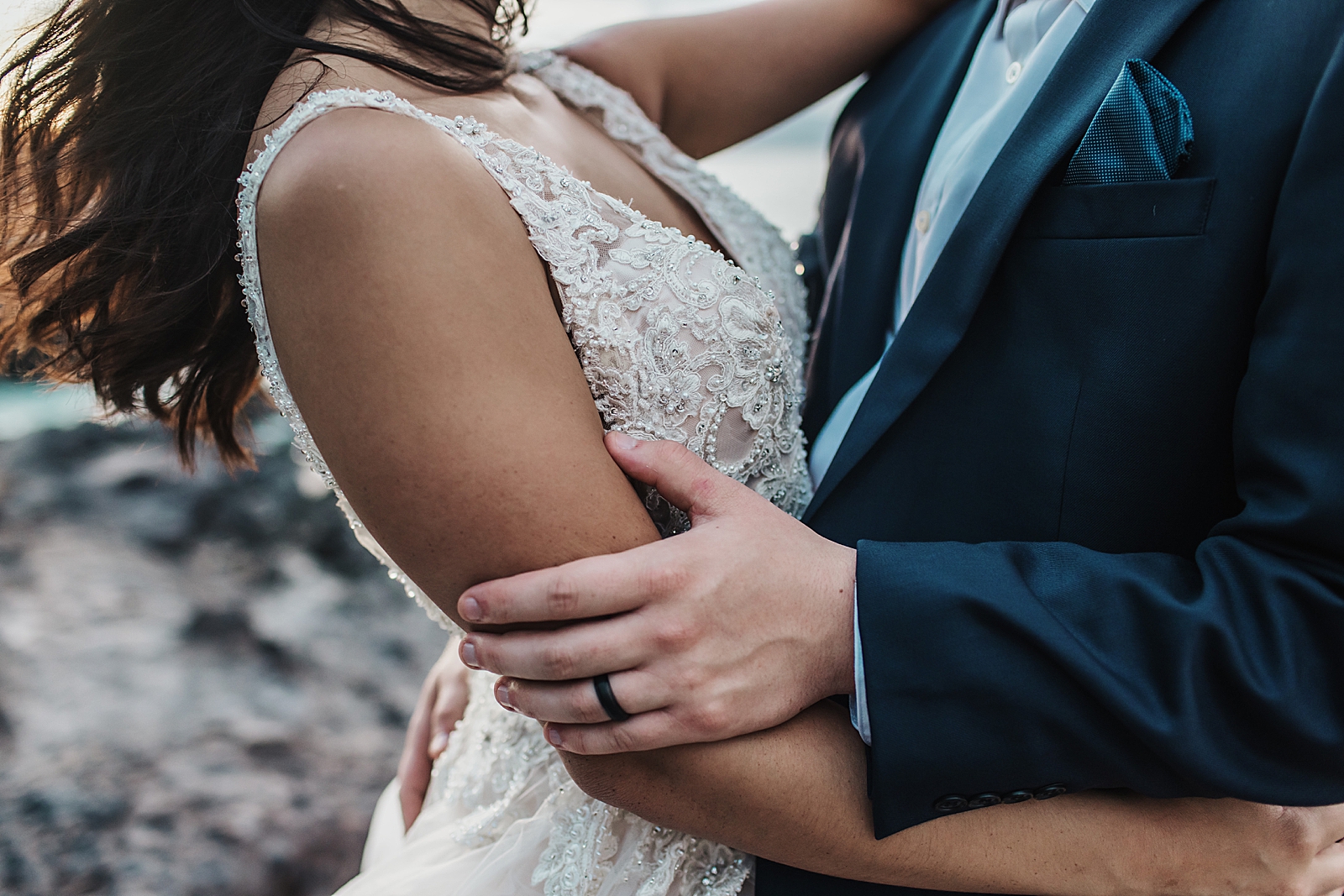 Closeup shot of Groom's hand on Bride's arm with black wedding band