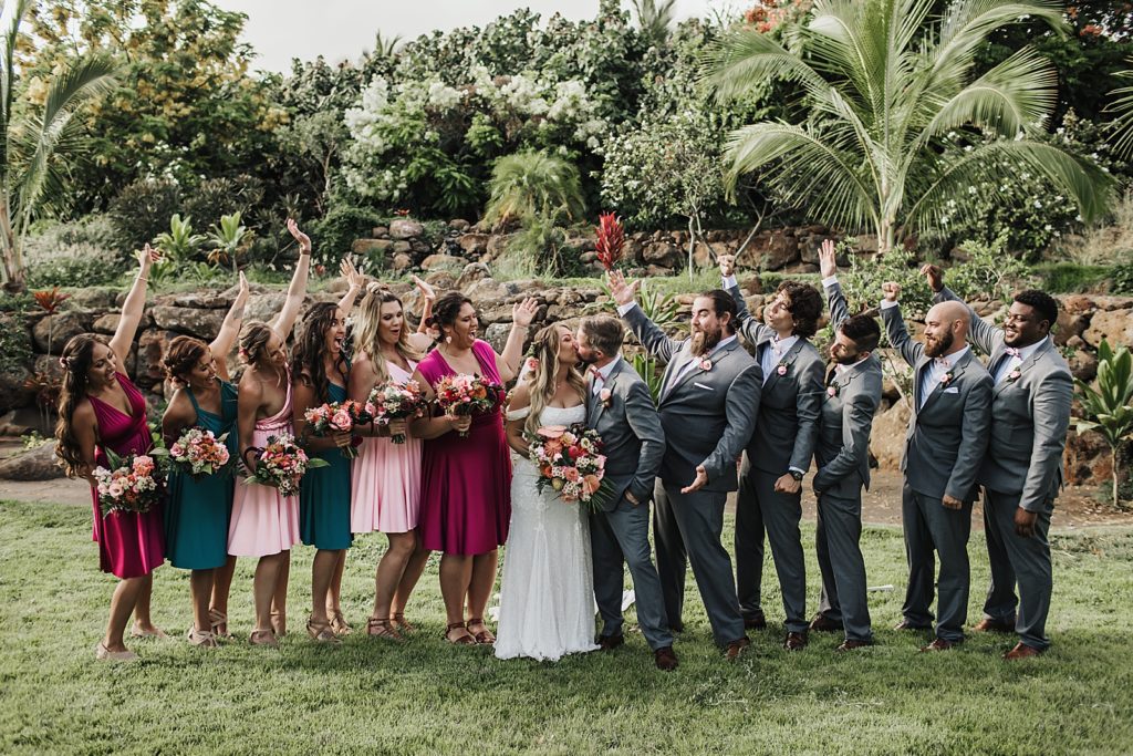 Bride and Groom kissing with wedding party celebrating next to them