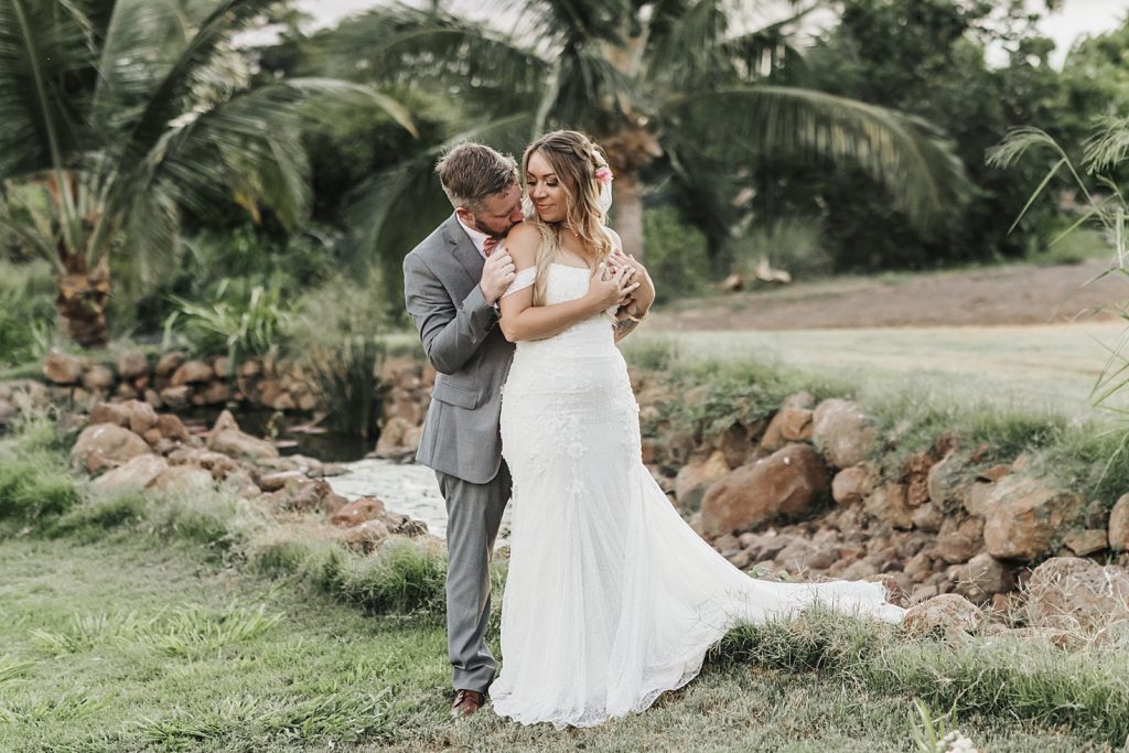 Groom holding Bride from behind and looking into her eyes outside