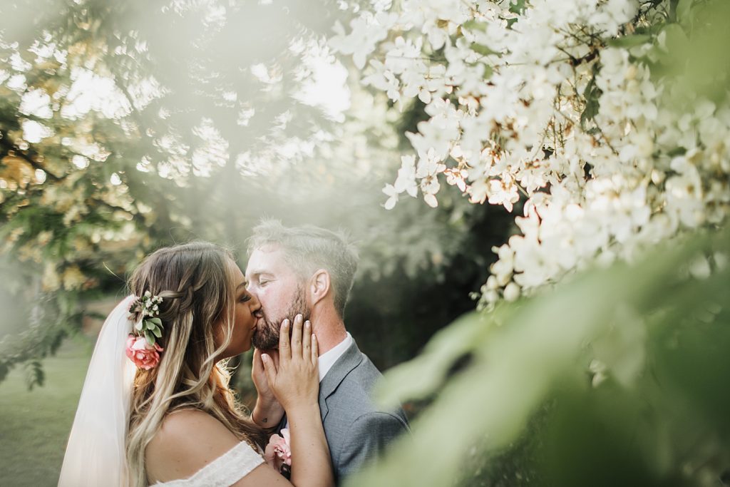 Bride and Groom kissing by branches with flowers