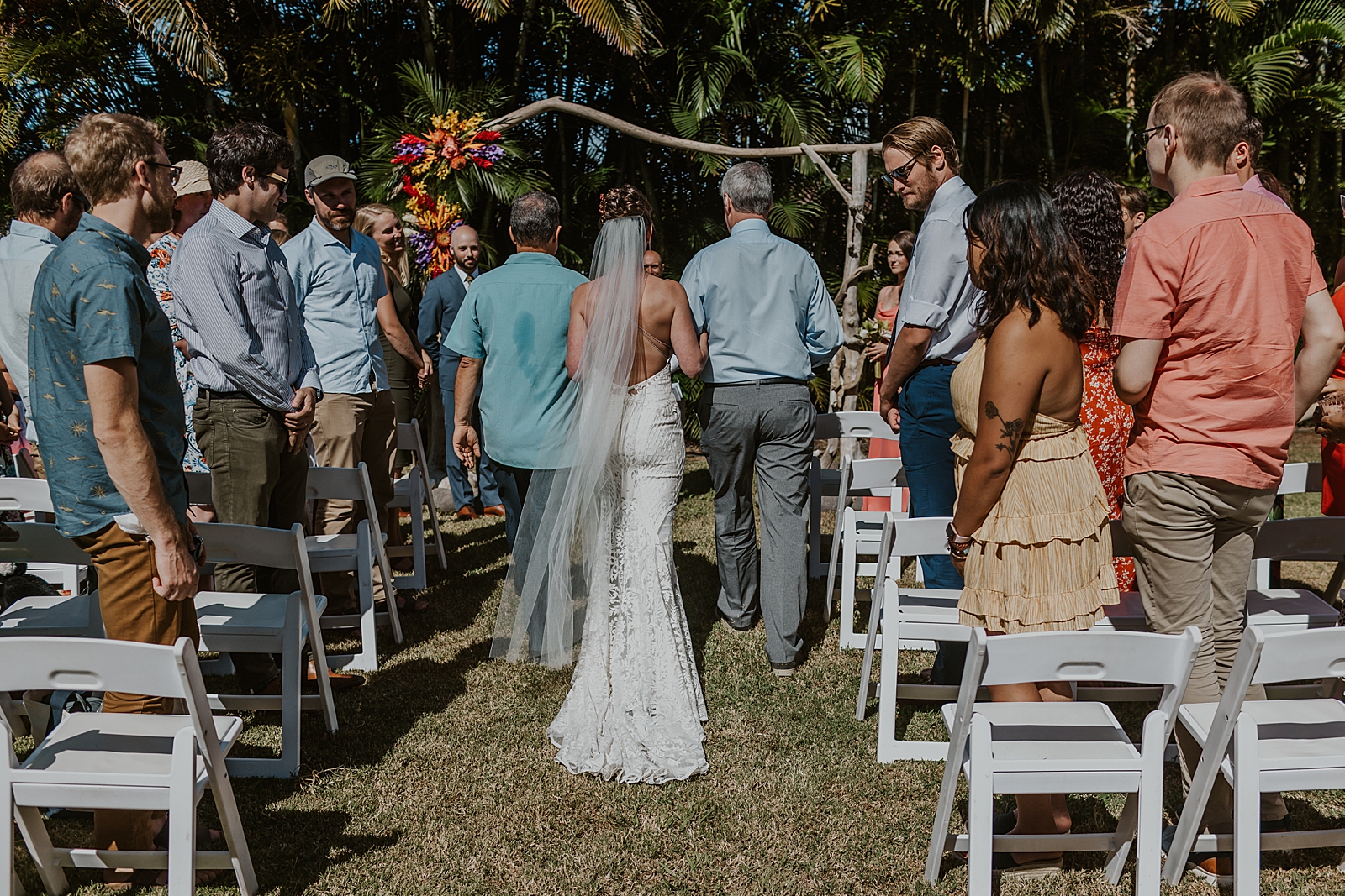 Bride entering outdoor Ceremony arm in arm with Fathers