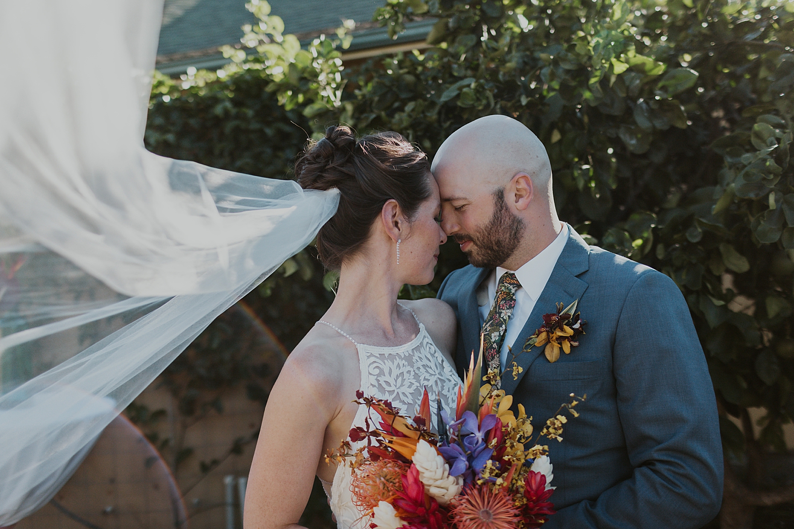 Bride and Groom resting their heads on each other by green hedge