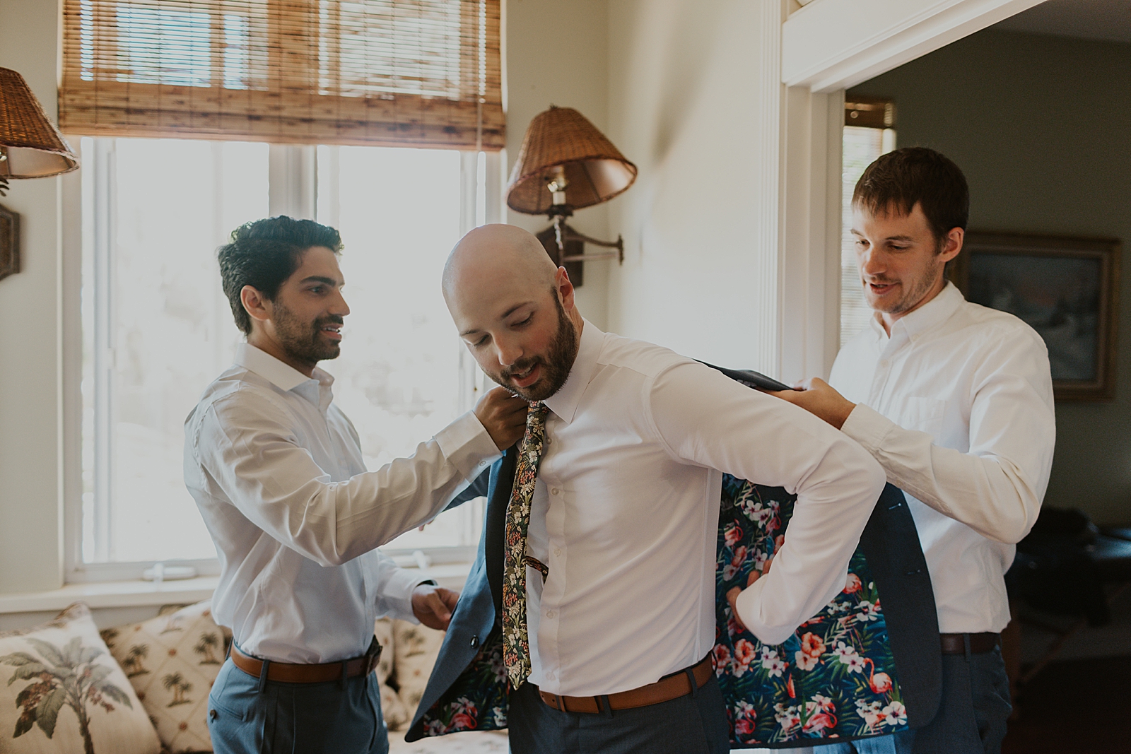 Groomsmen helping Groom put on floral interior jacket getting ready