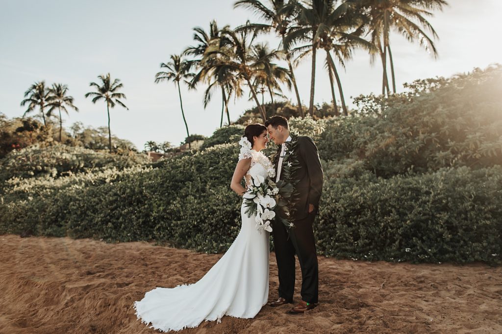 Bride and Groom resting their heads on each other standing on the sand with the sun setting