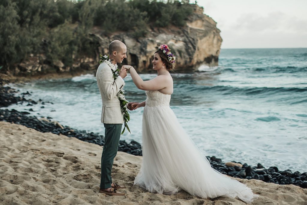 Bride and Groom holding hands by the side of the beach next to black rocks