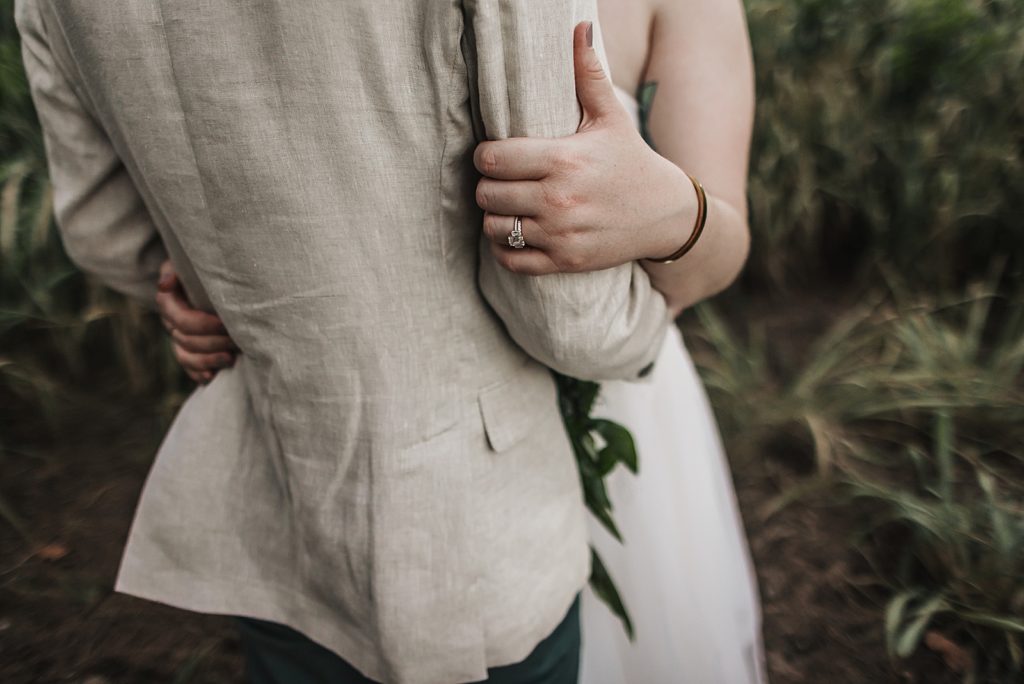 Closeup of Bride holding Groom's arm with wedding band and engagement ring