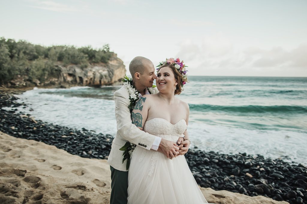 Groom hugging Bride from behind on the beach